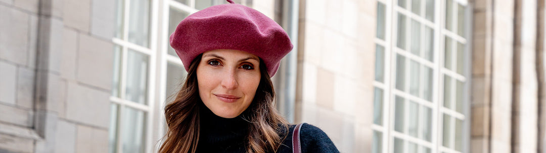 Frau mit Baskenmütze steht vor einem Haus mit hohen Fenstern