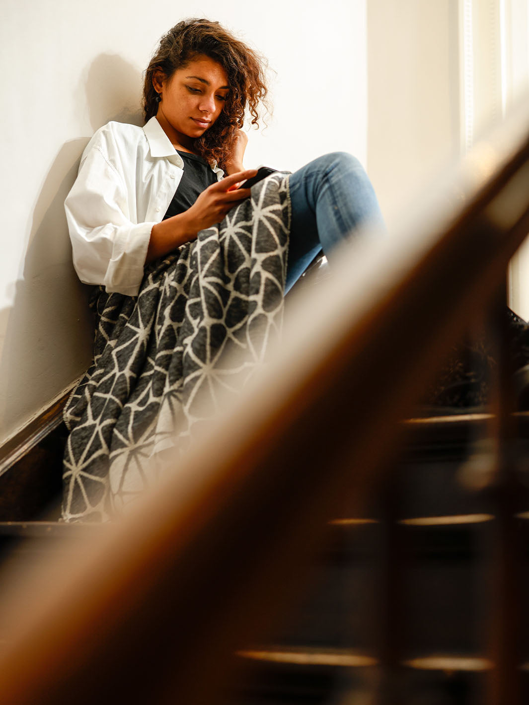 Eine Frau sitzt auf einer Treppe, hat sich in eine FRAAS Decke gekuschelt und liest