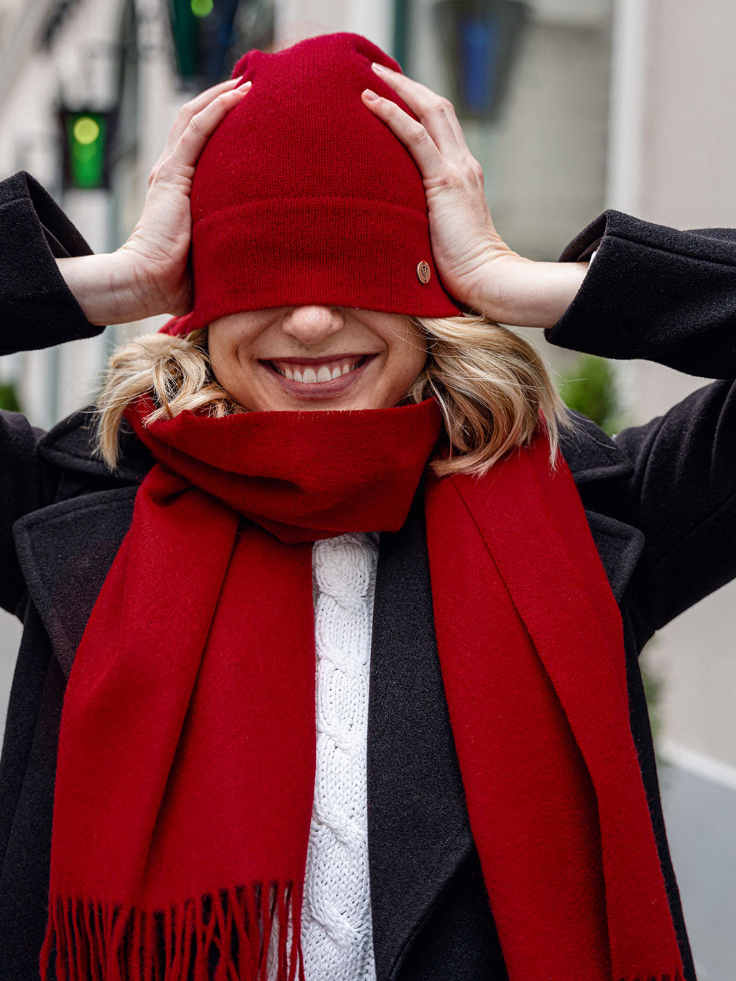 Lachende Frau hat mit rotem Schal und roter Mütze hat sich ihre Mütze über die Augen gezogen