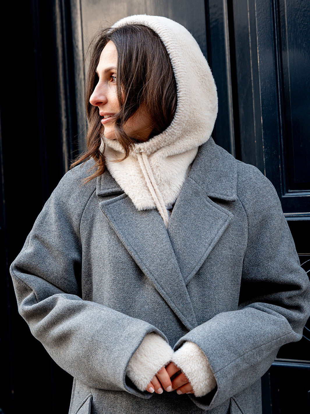 Frau mit LOEVENICH Balaklava 676005 und Stulpen 676008 steht vor einer Haustür und wartet