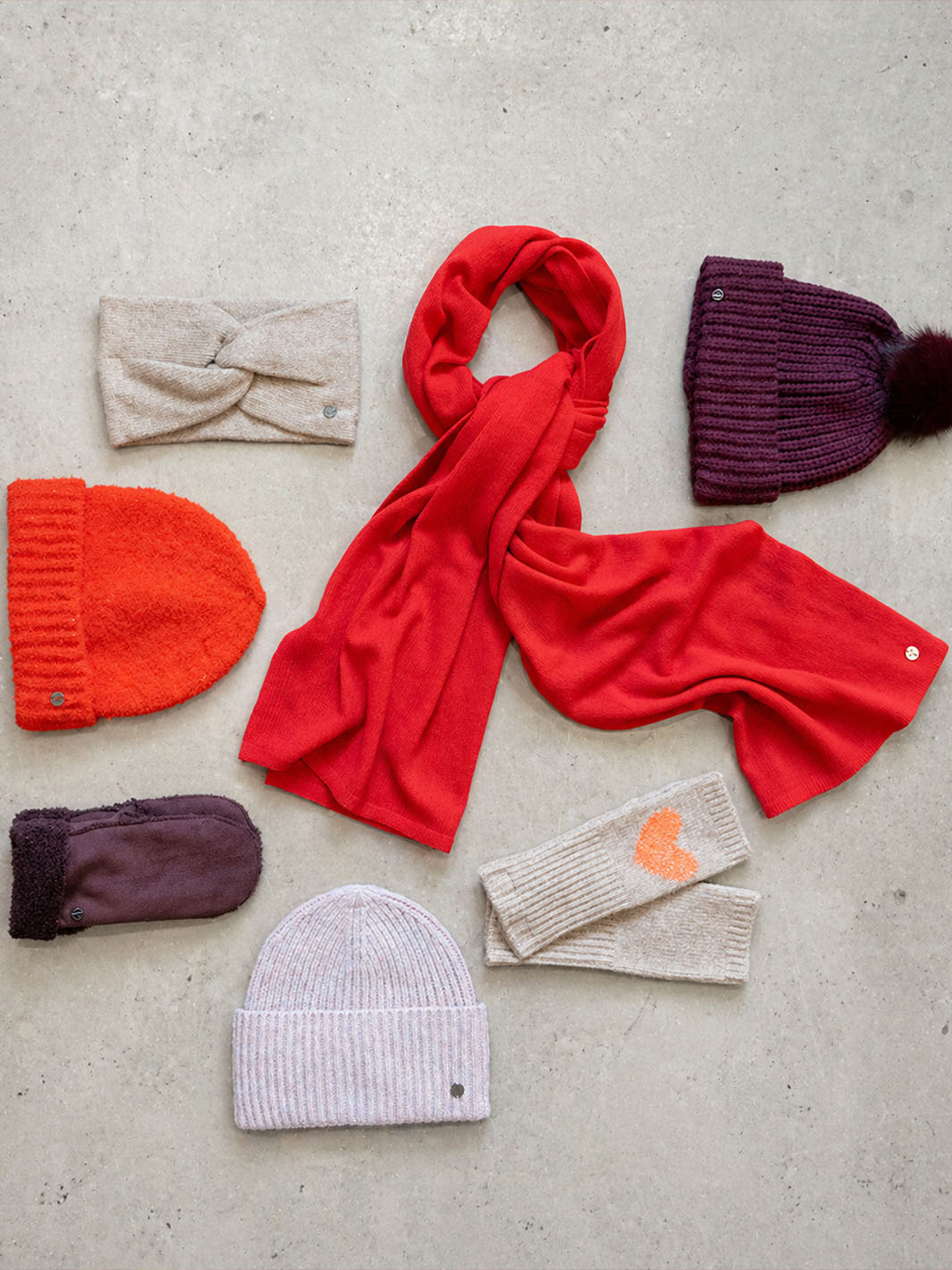 Zusammenstellung von Kopfbedeckungen, Schal und Handschuhen in Rot und Beige.