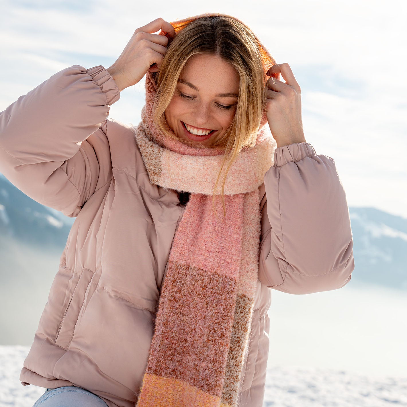 Frau im Schnee mit warmer Jacke wickelt sich ihren Schal um Hals und Kopf