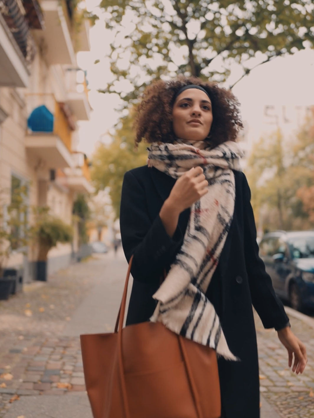Eine Frau mit dickem FRAAS Plaid Schal und Handtasche läuft durch die Stadt.