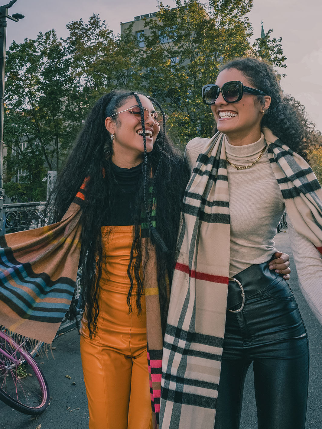 zwei Frauen haben sich eingehakt und laufen lachend über eine Brücke.
