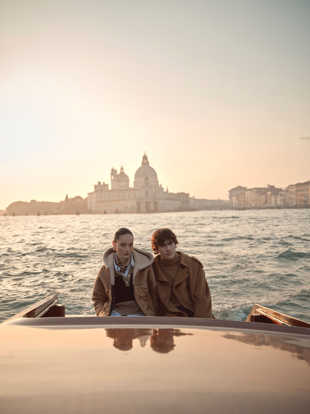 Eine Frau und ein Mann fahren mit einem Boot über die Lagune von Venedig, im Hintergrund alte Gebäude