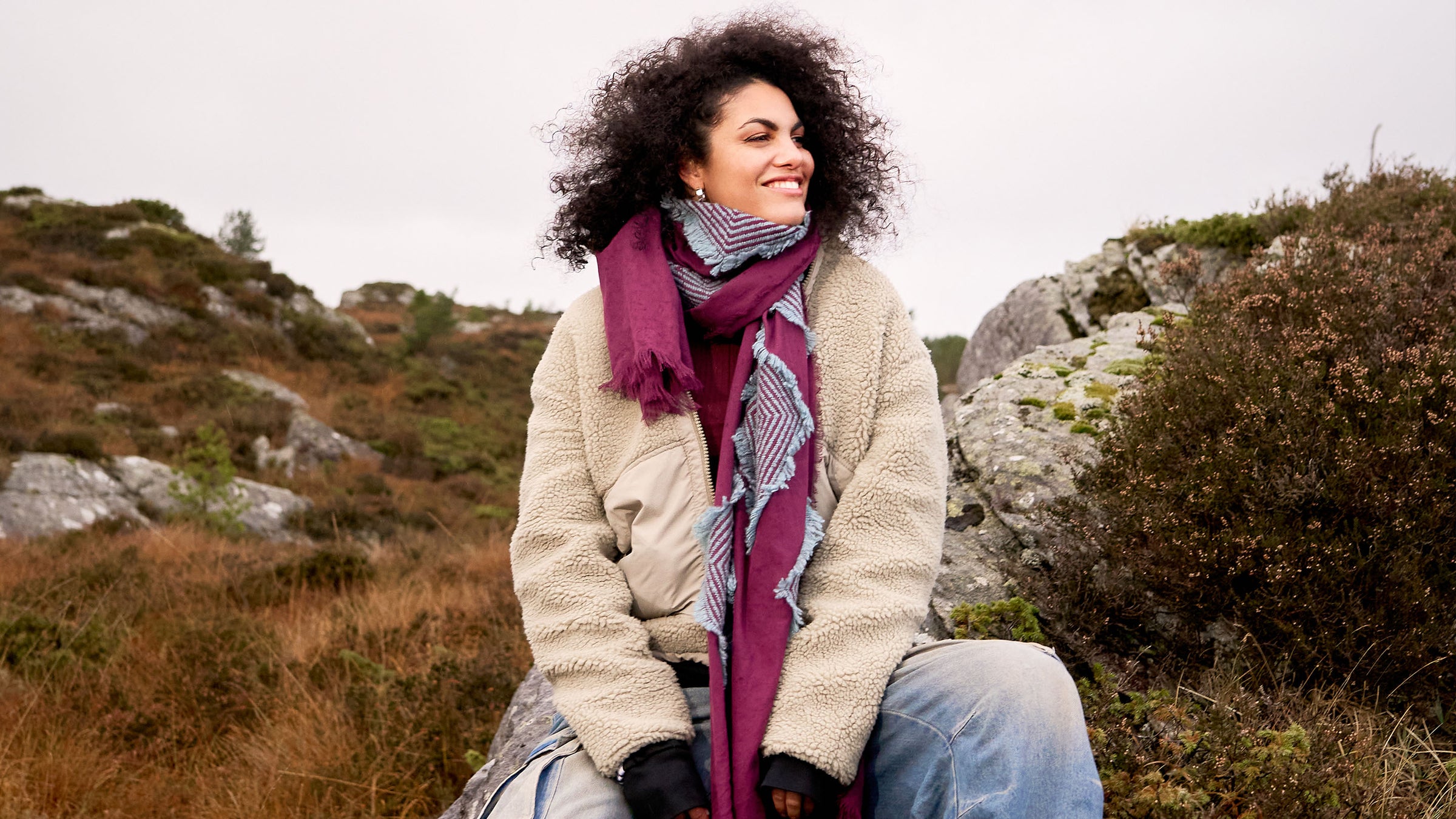Frau mit Fil Coupé Stola mit geometrischem Muster und warmer Jacke vor wilder Landschaft