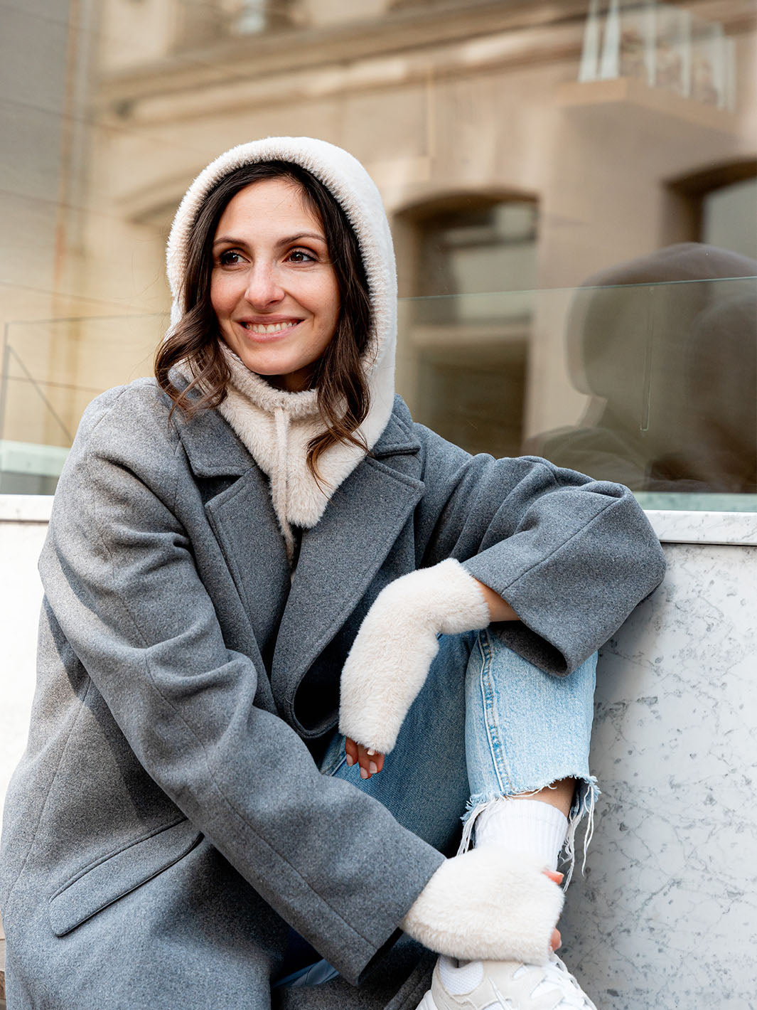 Frau sitzt auf einer Bank, am Kopf eine flauschige Balaklava, an den Händen die passenden Stulpen