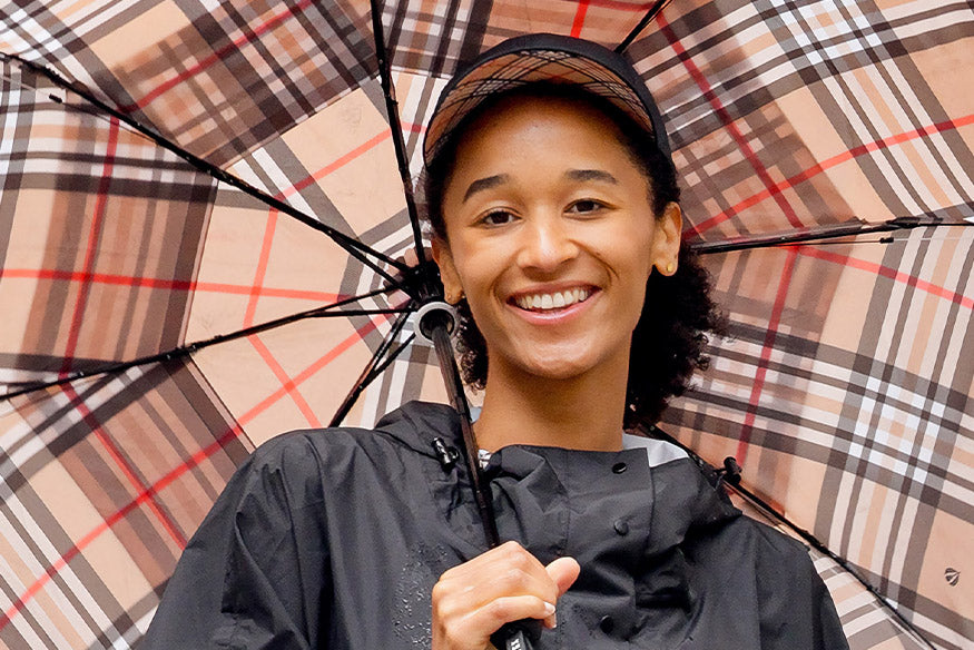 Frau steht unter einem karierten Regenschirm und lacht in die Kamera