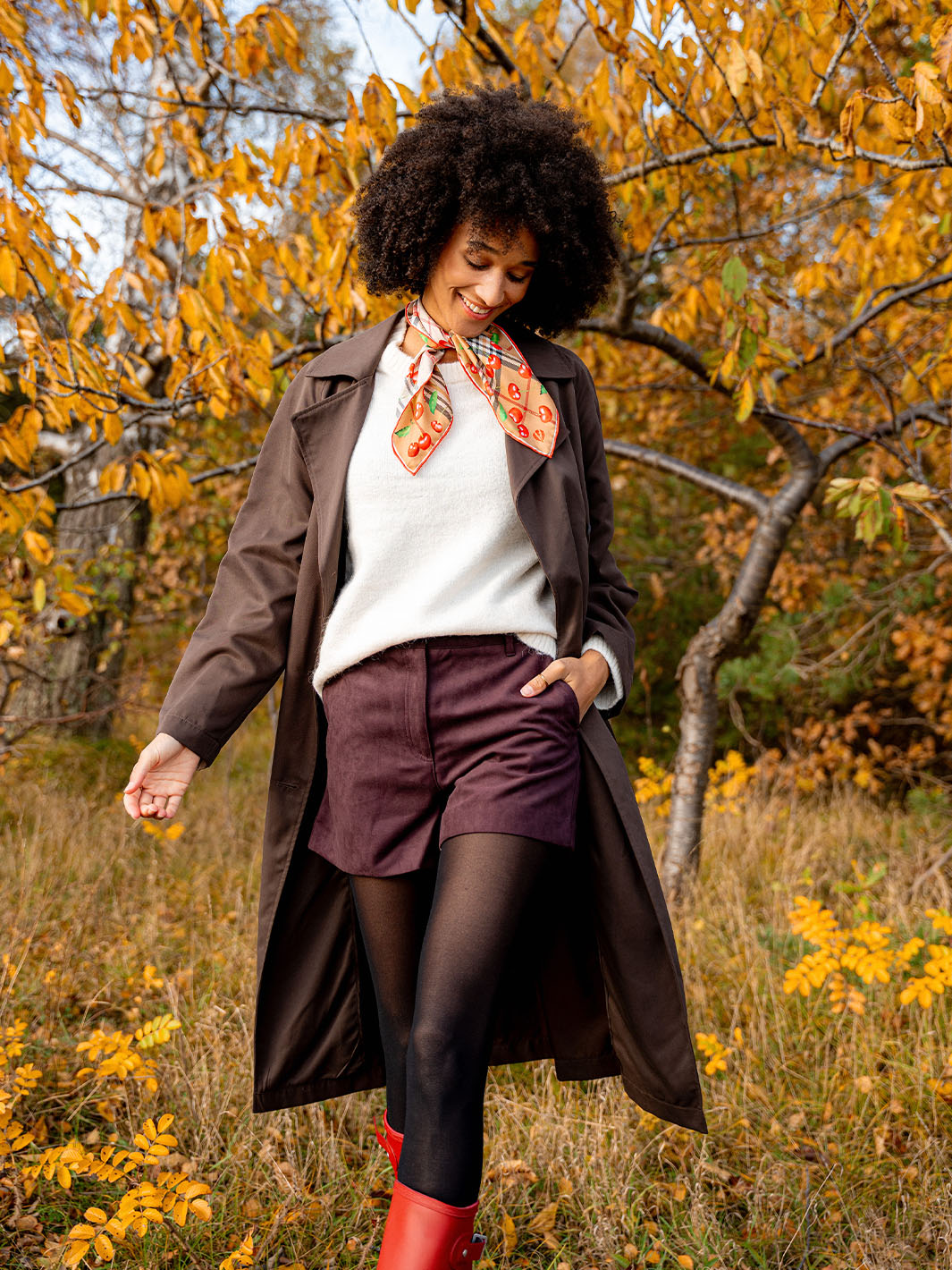 Frau mit Nickituch mit FRAAS Plaid Karo und Kirschen-Print aus reiner Seide läuft durch eine herbstliche Landschaft