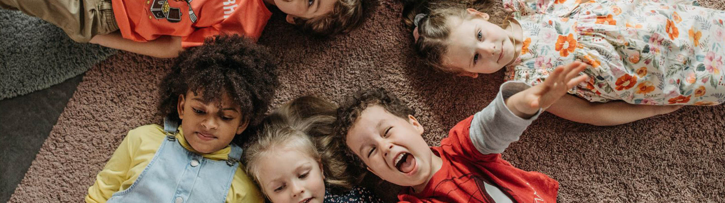Jungen und Mädchen liegen im Kreis auf dem Boden, manche sehen in die Kamera, ein Junge ruft etwas