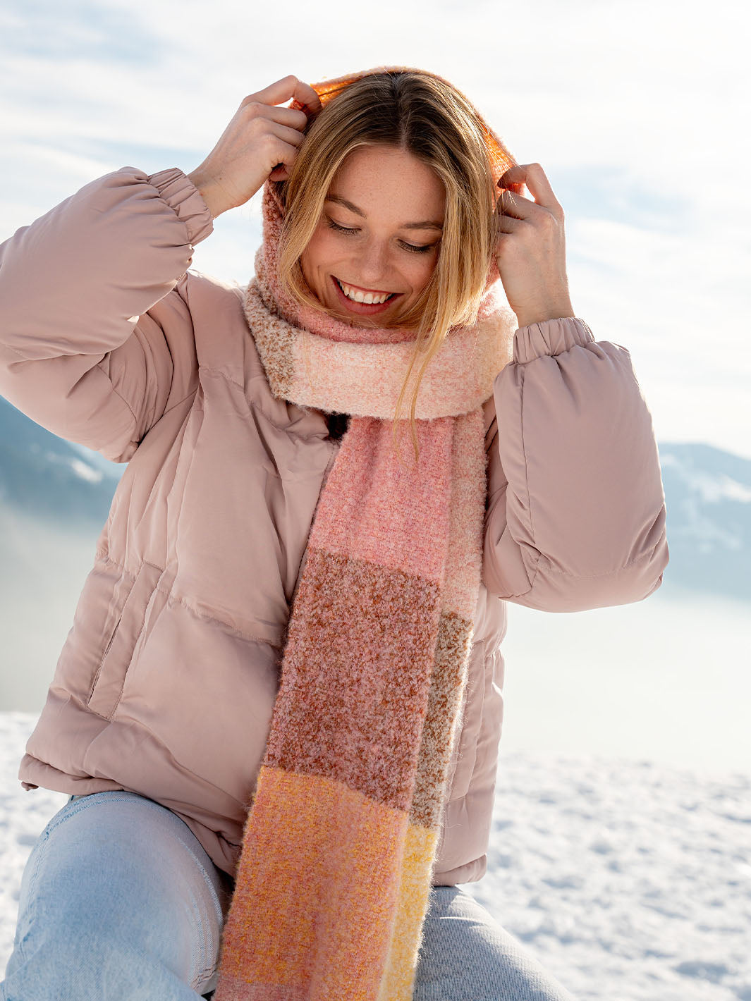 Frau im Schnee mit warmer Jacke wickelt sich ihren Schal um Hals und Kopf