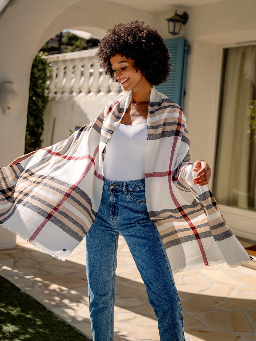 junge Frau hat sich die FRAAS Plaid Stola 631114 um die Schultern gelegt und tanzt auf der Terrasse 