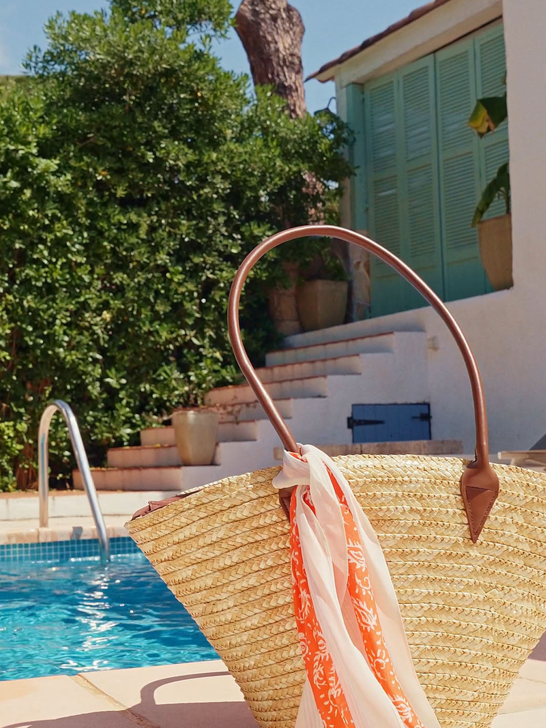 Eine Strandtasche, um deren Henkel ein Halstuch geknotet wurde, steht vor deinem Pool.