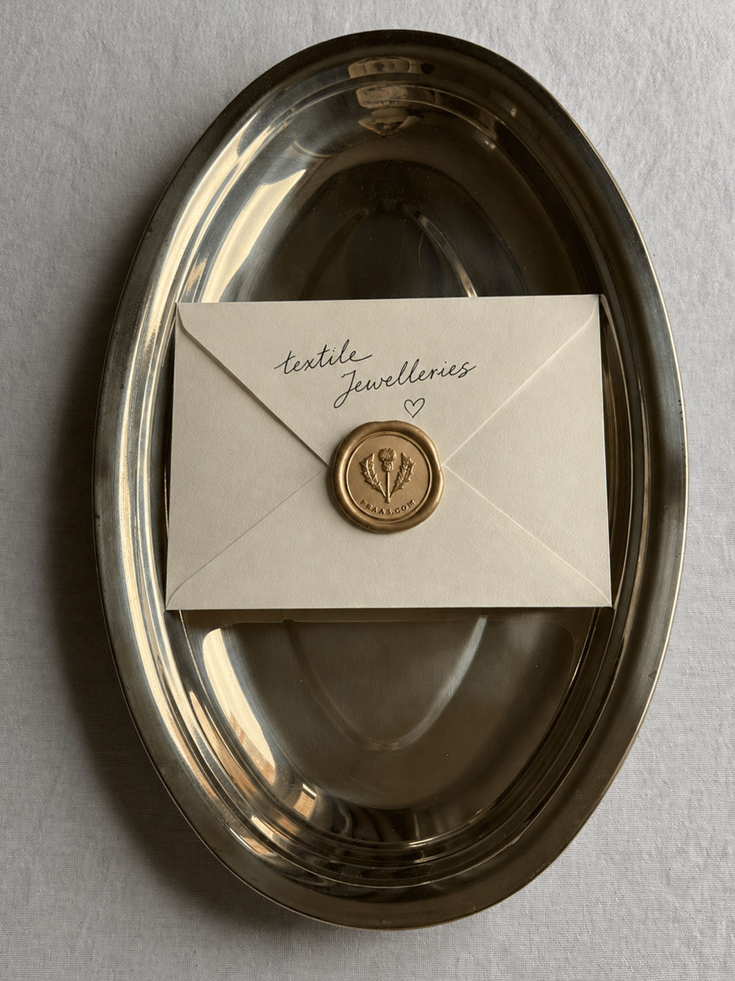 ein Briefumschlag mit der Aufschrift textile jewelleries und einem Wachssiegel liegt auf einem goldenen Tablett.