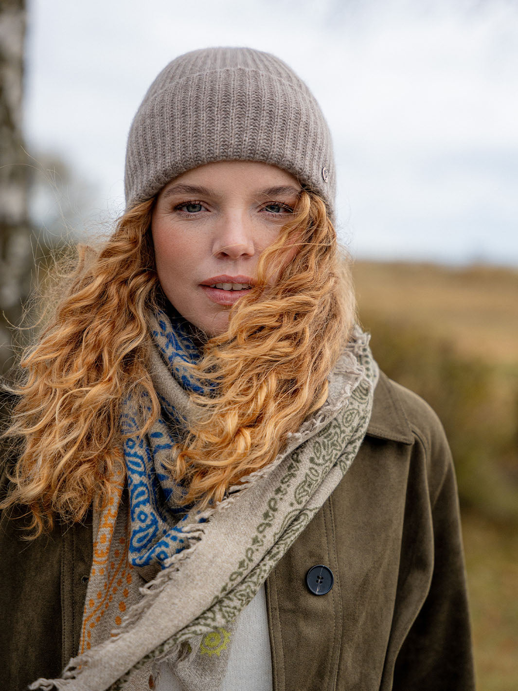 Frau in warmer Kleidung sieht in die Kamera. Der Wind weht durch ihr Haar.