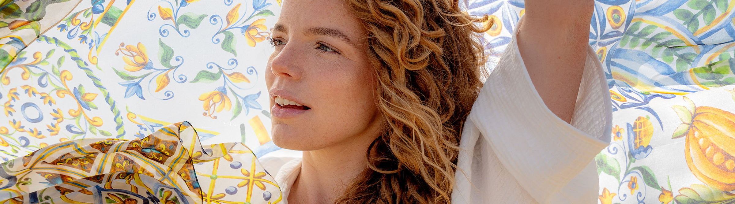 Frau hält die FRAAS Mosaik-Stola 622010 hinter sich und die Sonne wirft ihr Licht darauf.