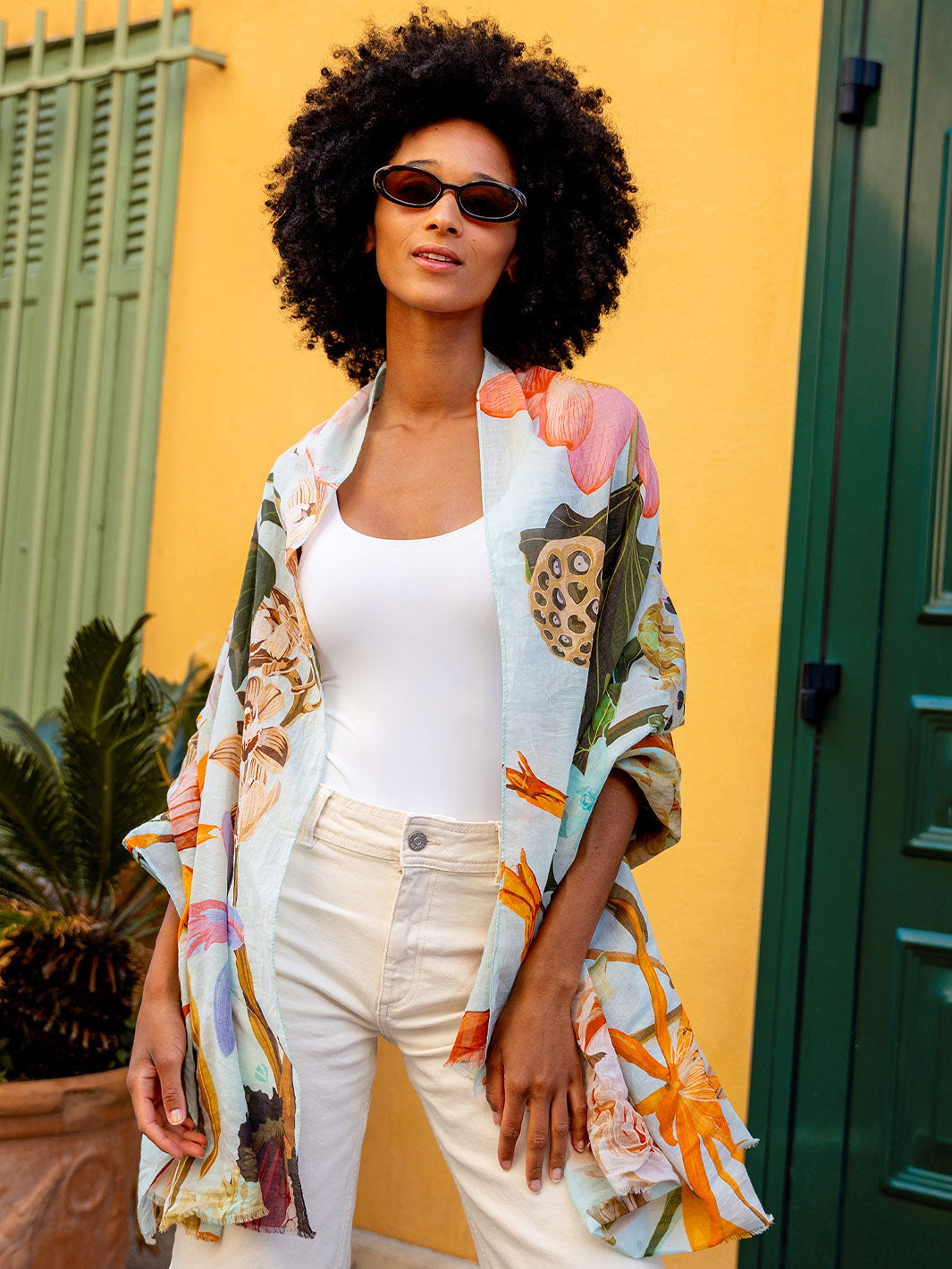 Frau mit Sonnenbrille und Seidenstola 609063 steht vor einer bunten Hauswand und Fensterläden und sieht in die Kamera.