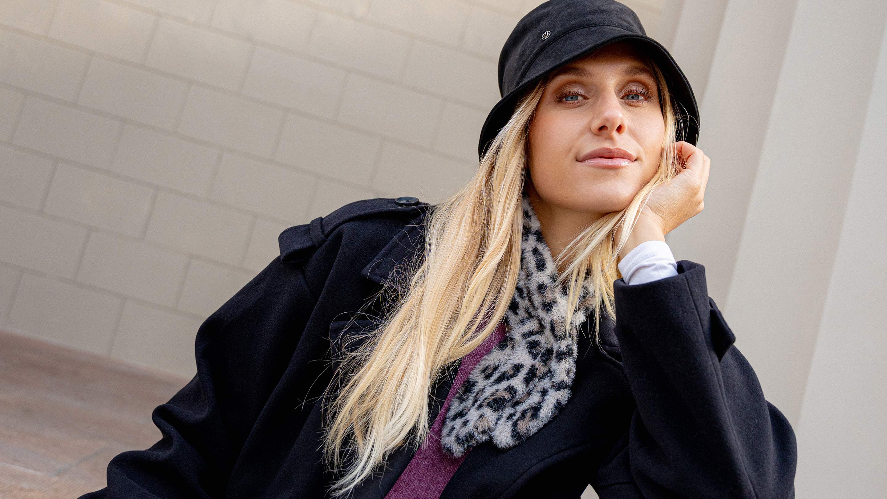 Frau mit Bucket Hat hat den Kopf in die Hand gestützt und sieht von oben in die Kamera