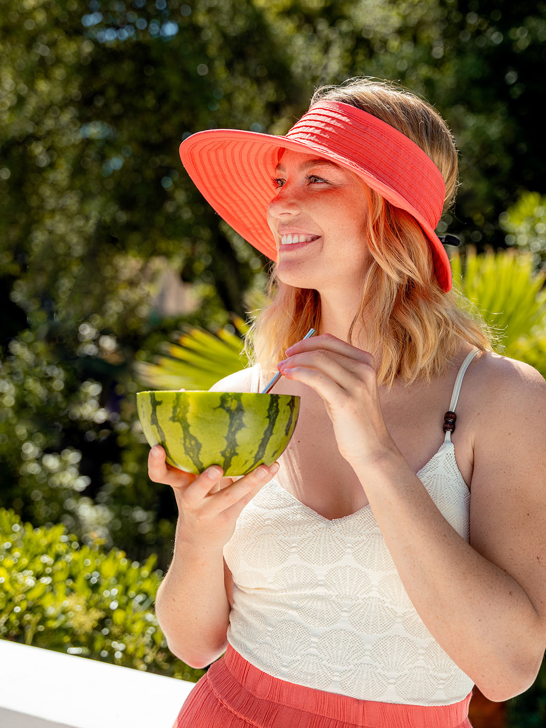 Frau in Sommerkleidung mit LOEVENICH Visor 672007 am Kopf trinkt mit dem Strohhalm etwas aus einer halben Wassermelone.