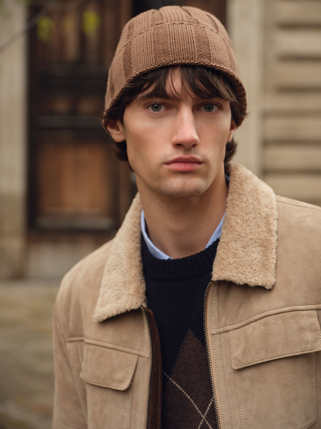 Mann mit Wintejacke und bugatti Beanie 
629326 steht vor einer Hauswand mit Gartentür.