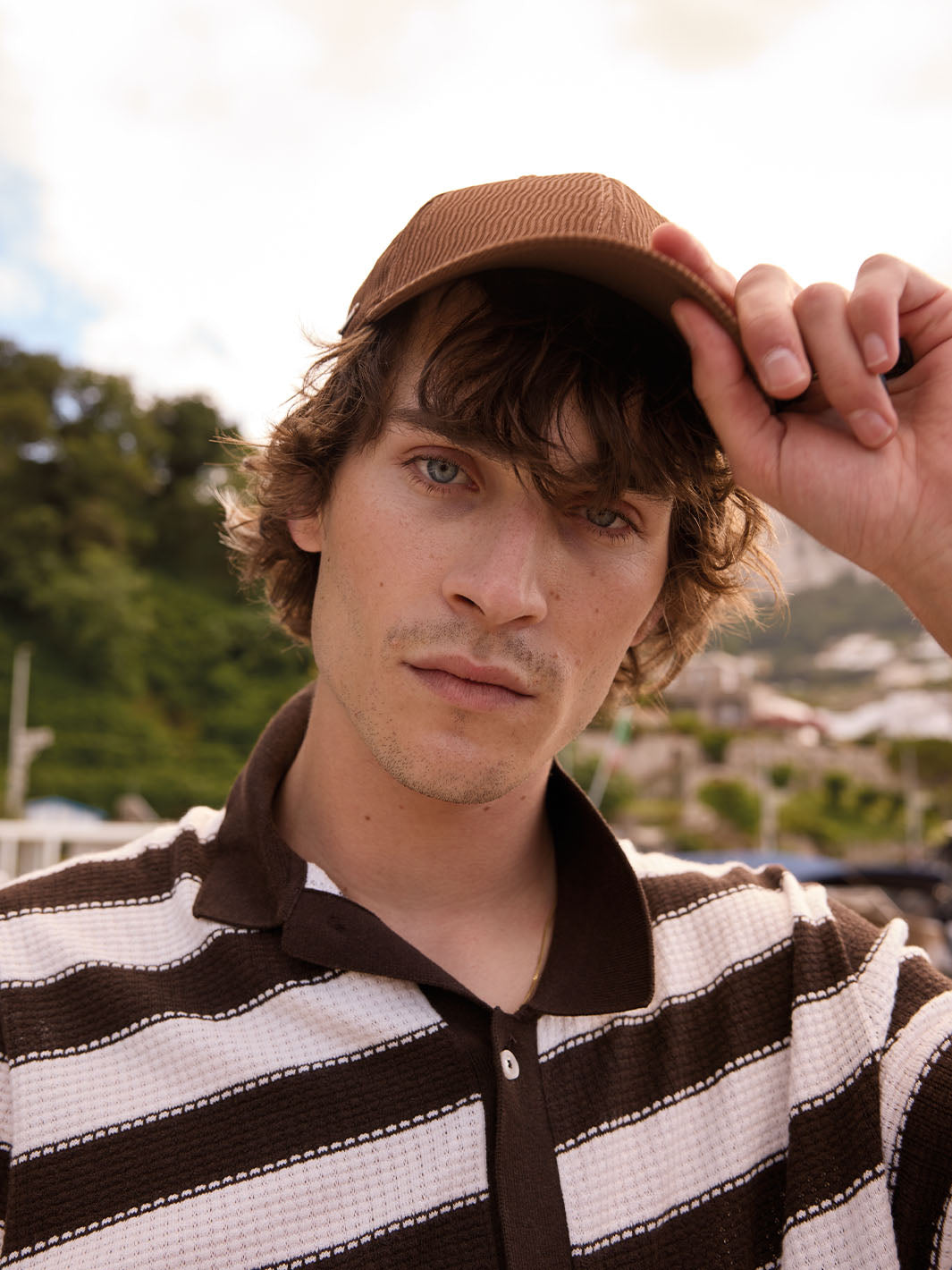 Nahaufnahme eines Mannes mit bugatti Baseballkappe vor Bäumen und Gebäuden