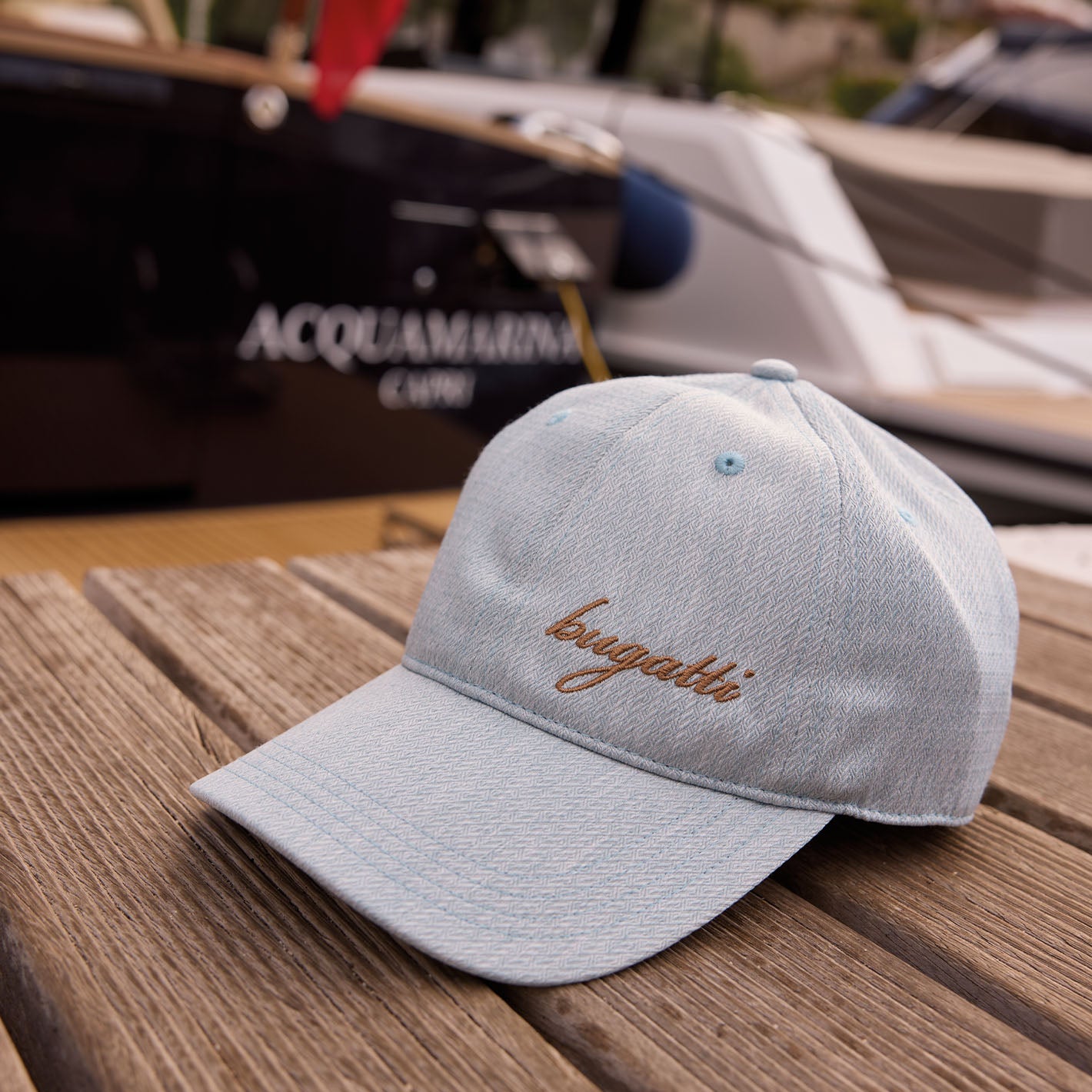 bugatti Baseballkappe liegt auf einem Holzsteg, im Hintergrund ist die Wand eines Boots zu sehen.