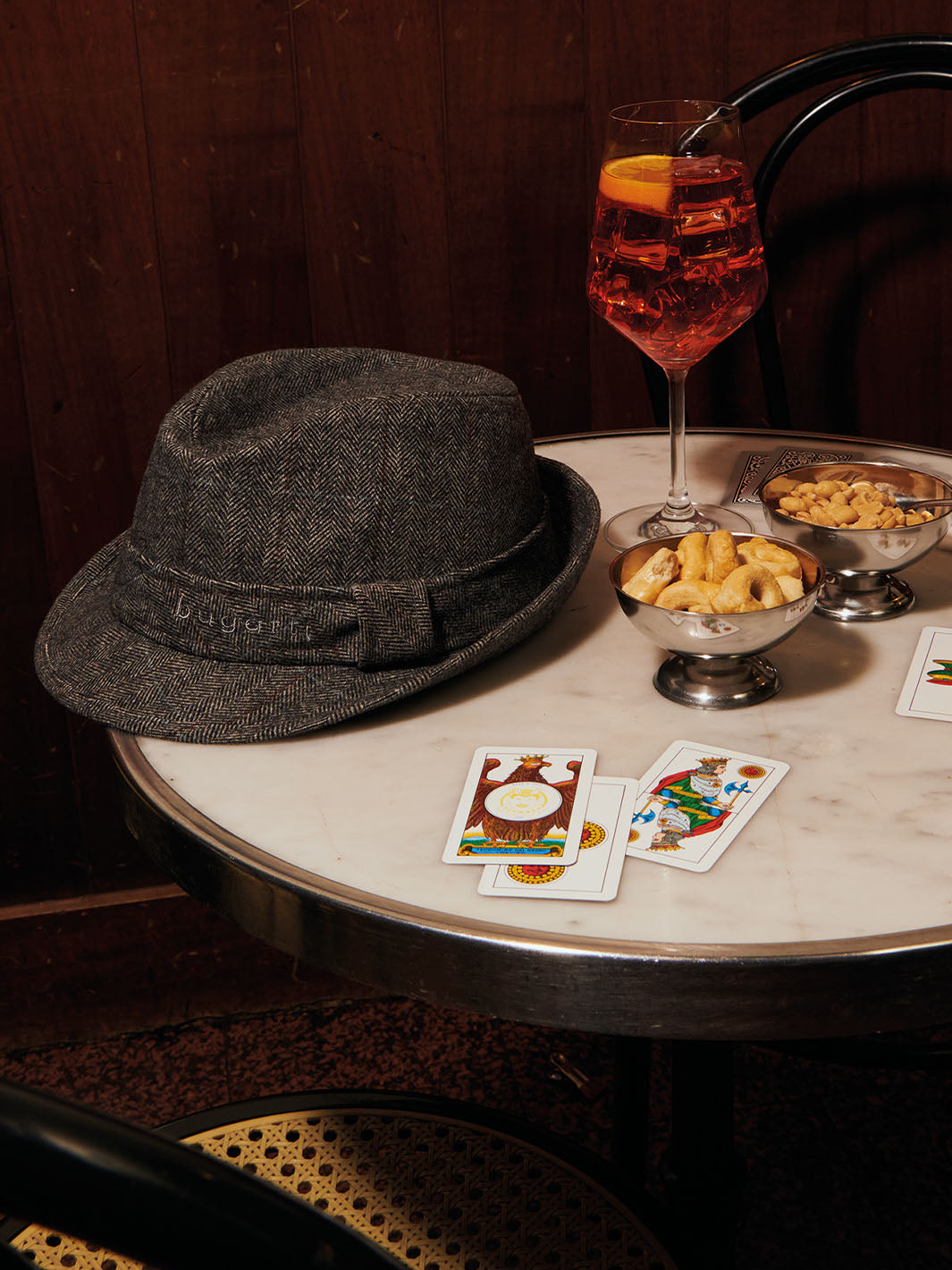 ein bugatti Hut 629027 liegt auf einem Tisch neben Spielkarten, Knabbereien und einem Getränk