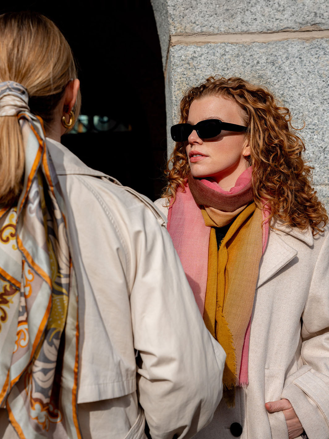 Frau mit Sonnenbrille steht vor einer Hauswand in der Sonne