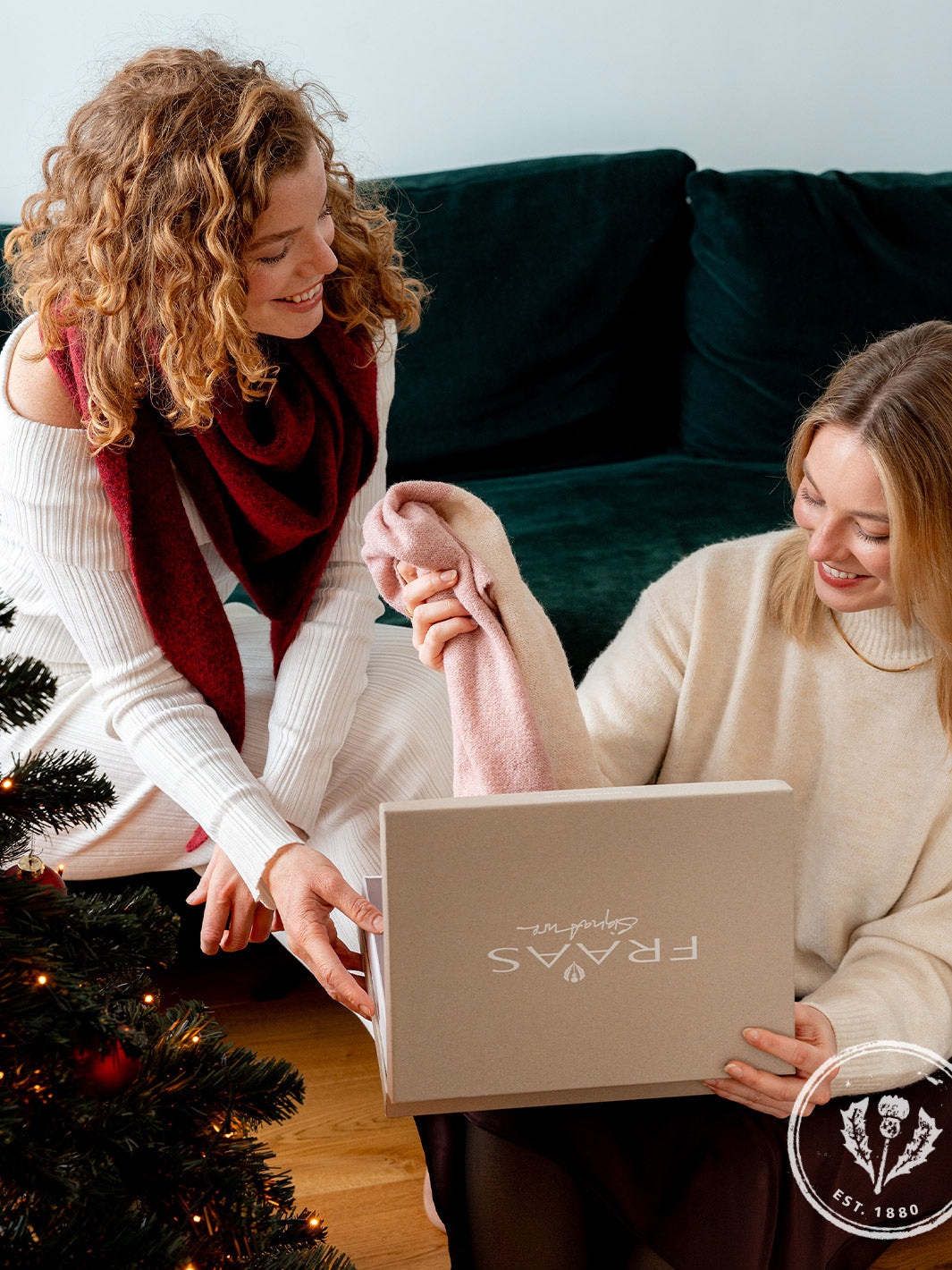 zwei Frauen sitzen am Sofa und holen einen Schal aus einer Geschenkbox