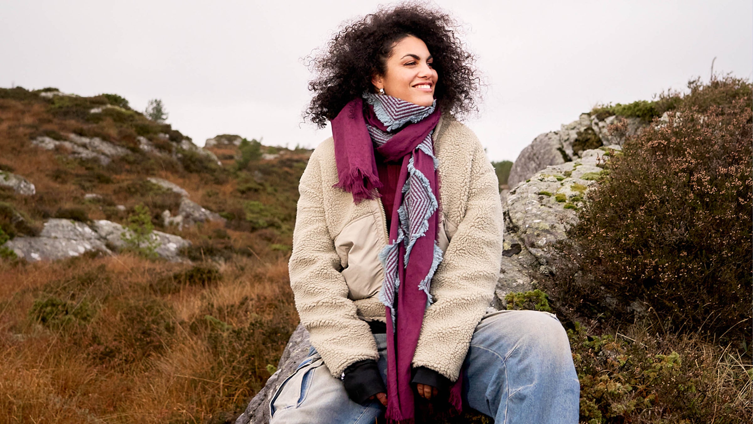 Frau mit Winterschal und kuschelgier Jacke vor Landschaft mit Felsen und Heidekraut