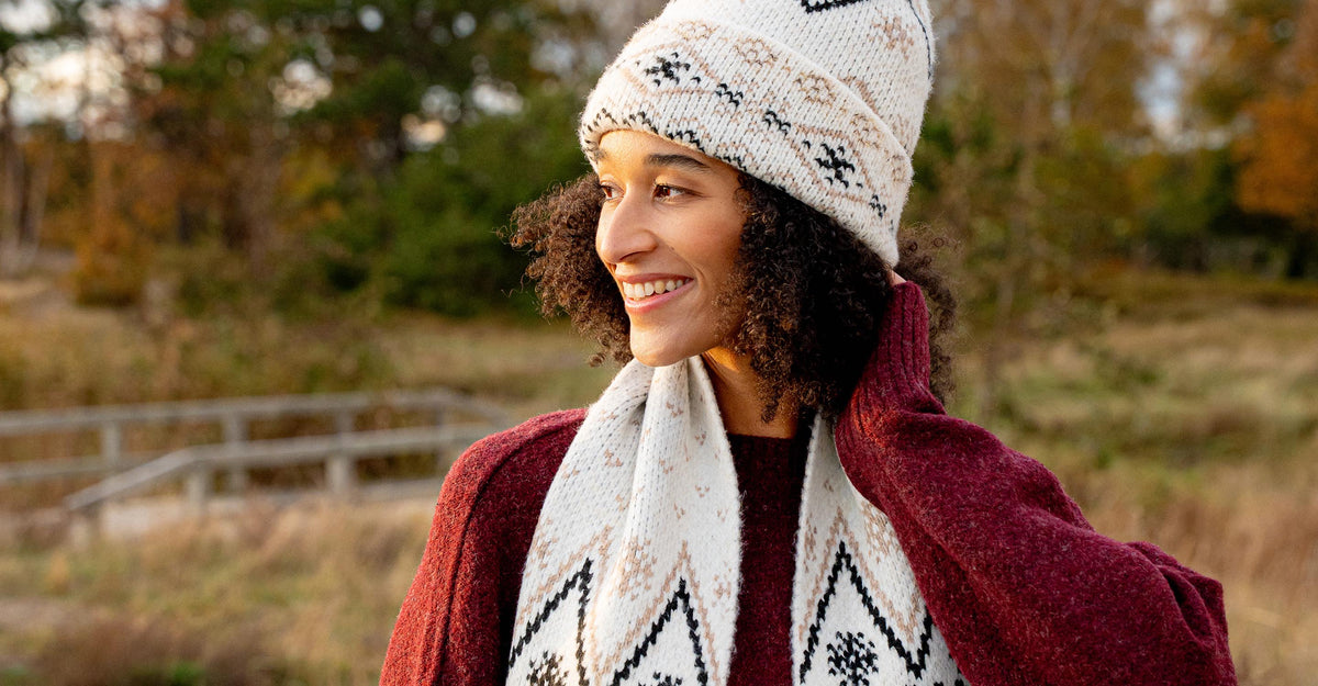 Frau mit Wintermütze und -schal läuft lächelnd durch eine herbstliche Landschaft