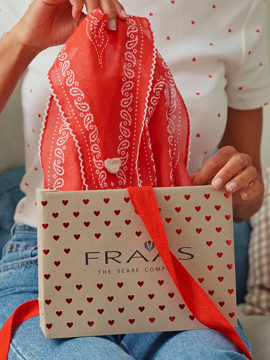 eine frau zieht das FRAAS Nickituch 609065 aus einer Geschenktasche mit Herzen