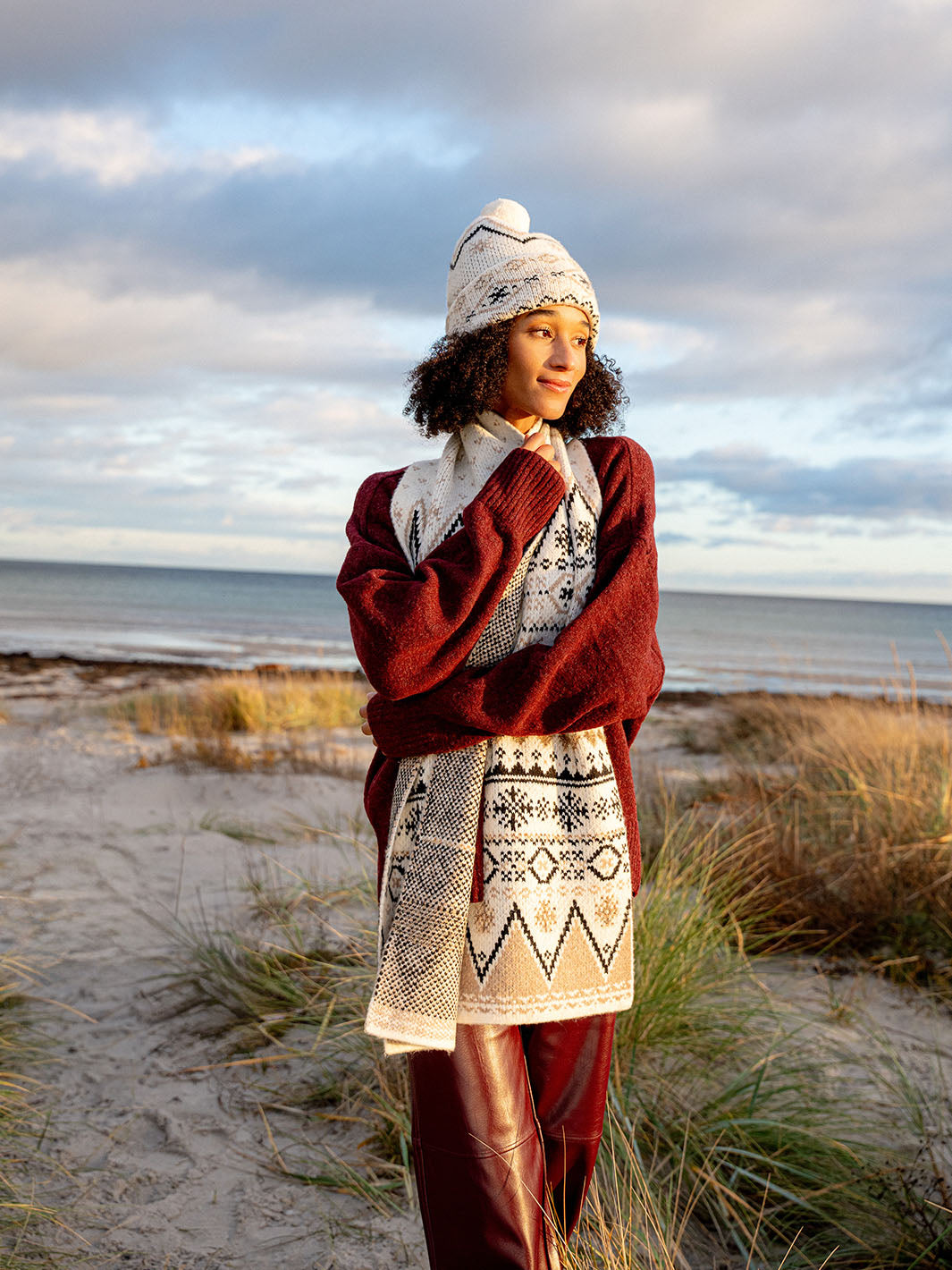 Frau mit Wintermütze und Schalläuft durch Dünen, im Hintergrund ist das Meer zu sehen.